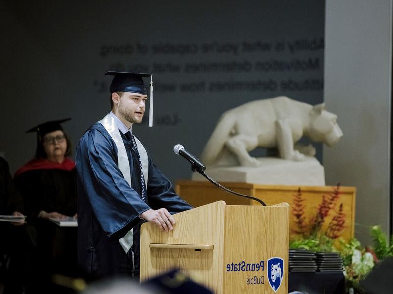 Male student in cap and gown giving a speech at commencement.