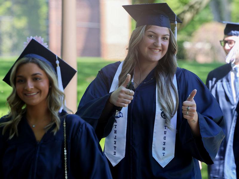 Two women are walking outside wearing commencement caps and gowns.