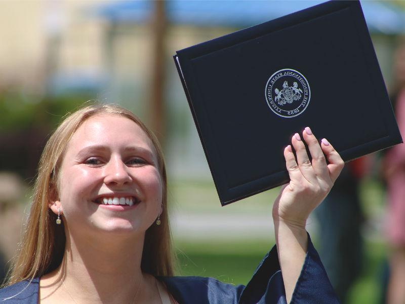 Penn State graduate holds up diploma and smiles while outdoors