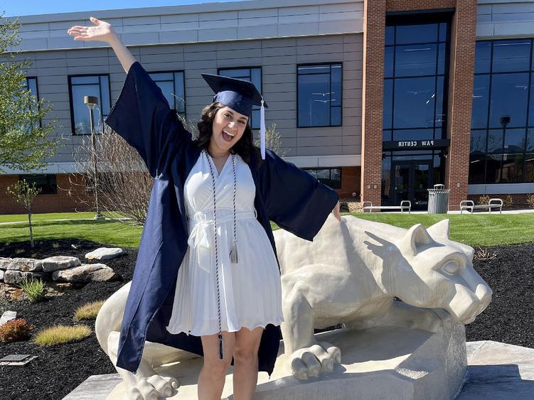 New Penn State graduate Anna Raffeinner celebrates with a joyful expression with the Lion Shrine on the Penn State DuBois campus, just outside the PAW Center